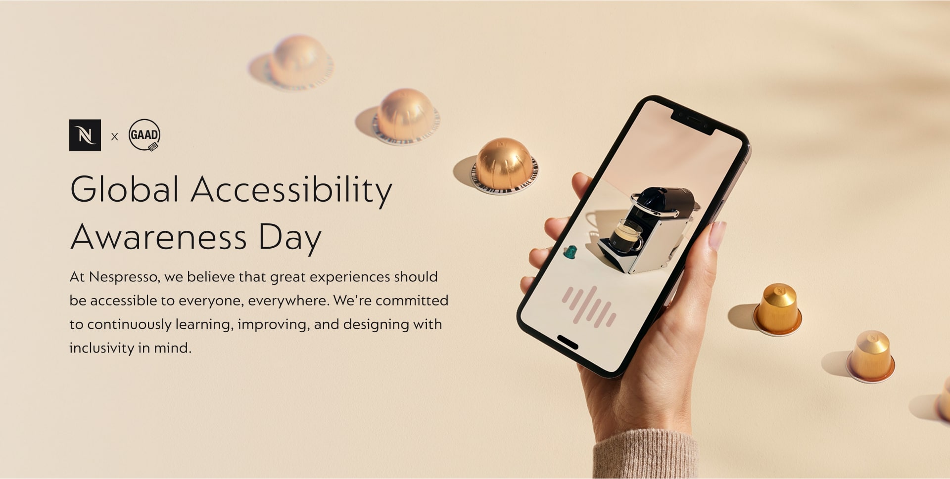 Nespresso marketing image celebrating Global Accessibility Awareness Day (GAAD). Text reads: Global Accessibility Awareness Day. At Nespresso, we believe that great experiences should be accessible to everyone, everywhere. We're committed to continuously learning, improving, and designing with inclusivity in mind. The image shows a hand holding a smartphone displaying a Nespresso coffee machine on the screen, surrounded by several gold and bronze Nespresso coffee capsules on a light-colored background.